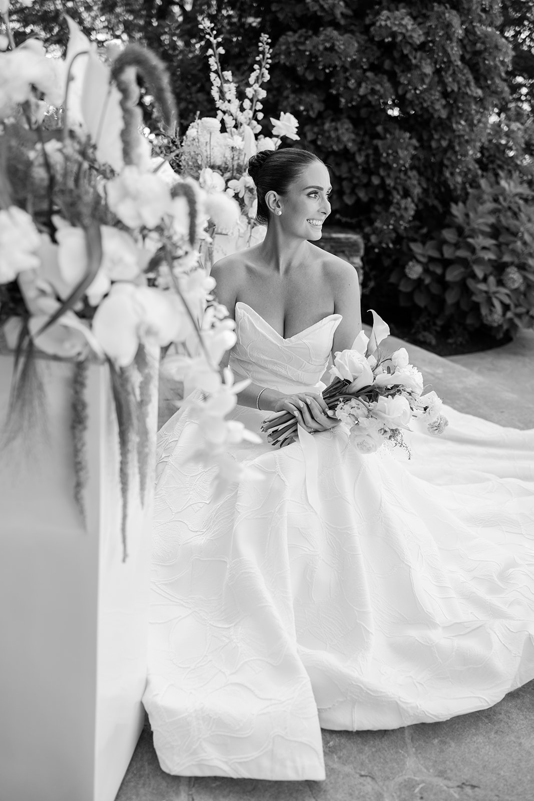 Black and white film photo of the bride sitting gracefully on stone steps and smiling warmly.
